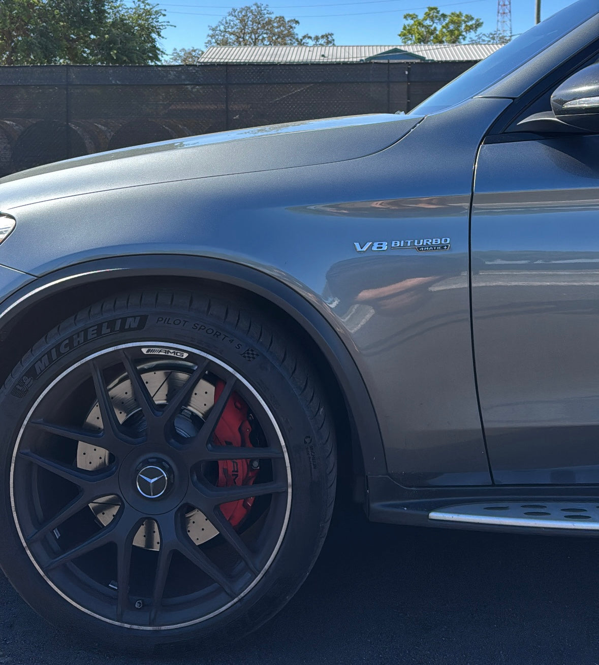 Close-up of grey Mercedes-Benz AMG SUV front wheel with black alloy rim, red brake caliper, and V8 Biturbo 4MATIC badge, showcasing luxury performance tires.
