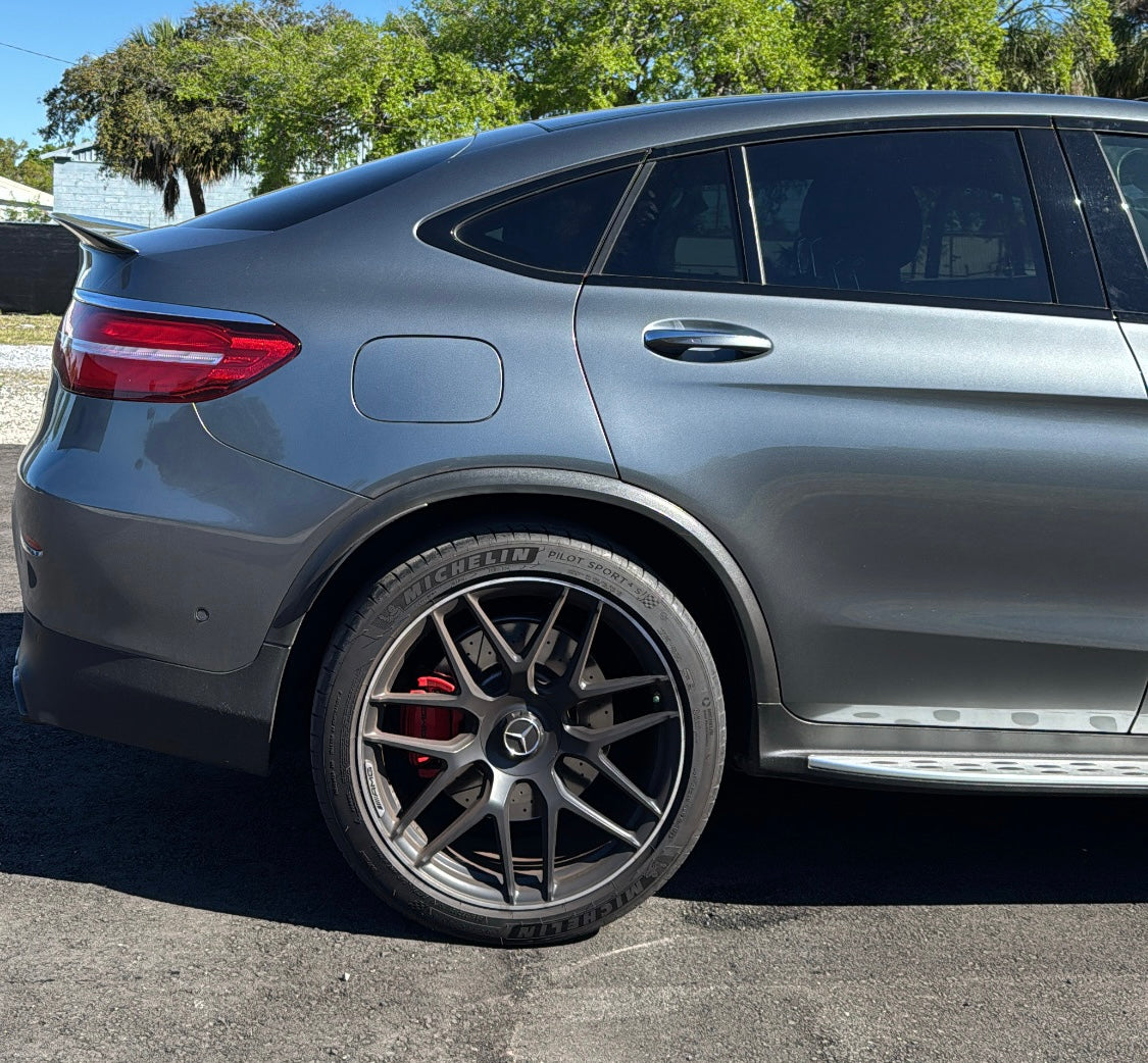 Rear side view of gray Mercedes-Benz SUV with Michelin Pilot Sport tires and black AMG alloy wheels on asphalt road.