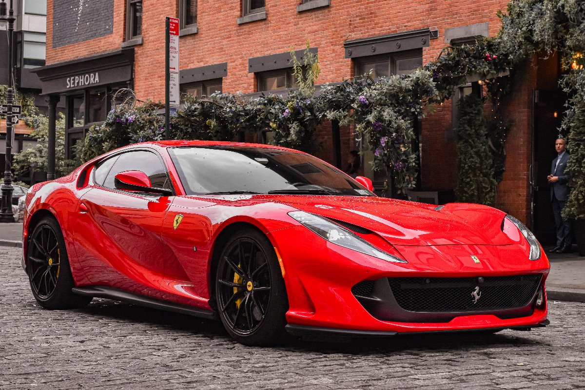 Red Ferrari 812 Superfast sports car with sleek aerodynamic design, black alloy wheels, and iconic Ferrari logo parked on a city street.
