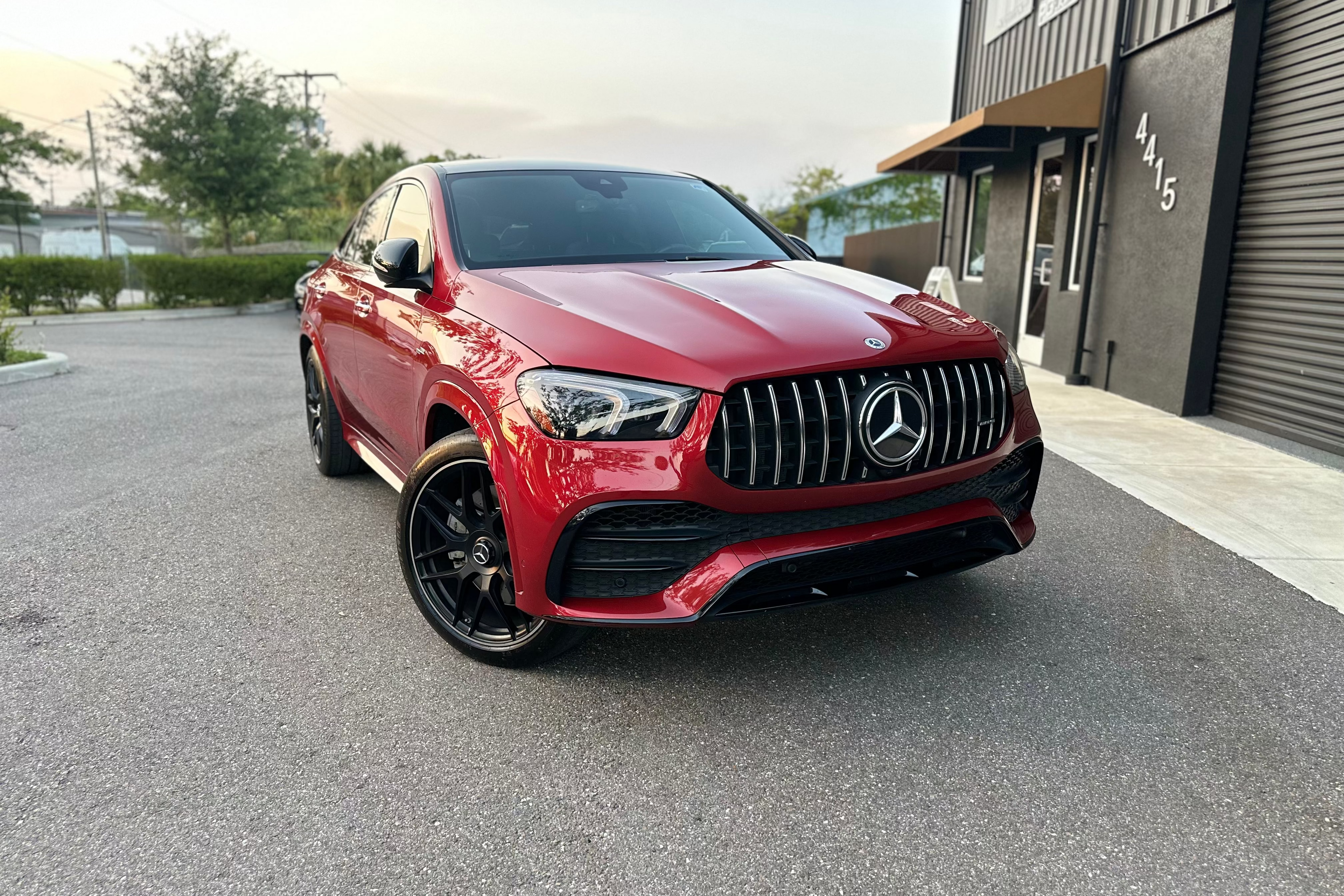 Red Mercedes-Benz luxury SUV with black alloy wheels parked outside modern building, showcasing sleek design and premium exterior.