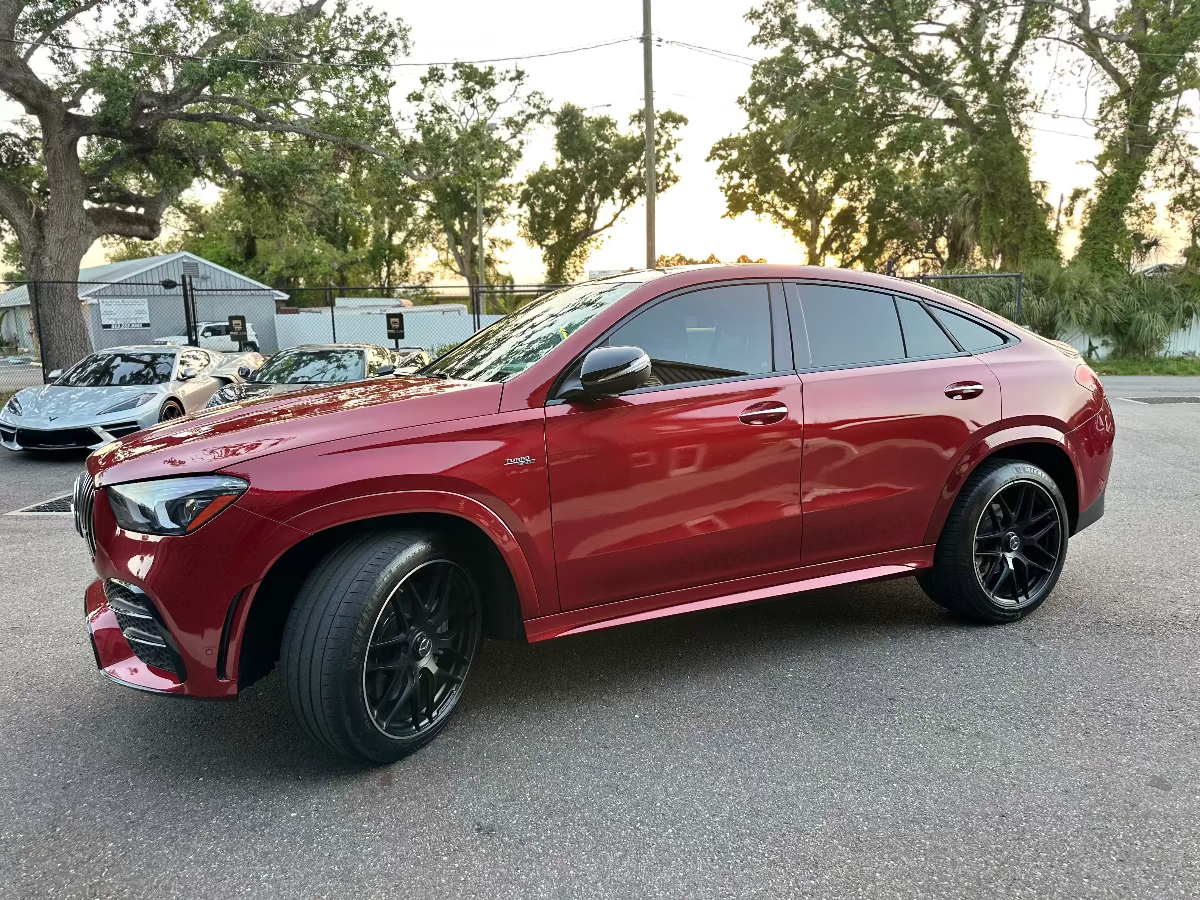 Red luxury Mercedes-Benz AMG GLE Coupe with black alloy wheels, sleek design, and tinted windows parked outdoors.