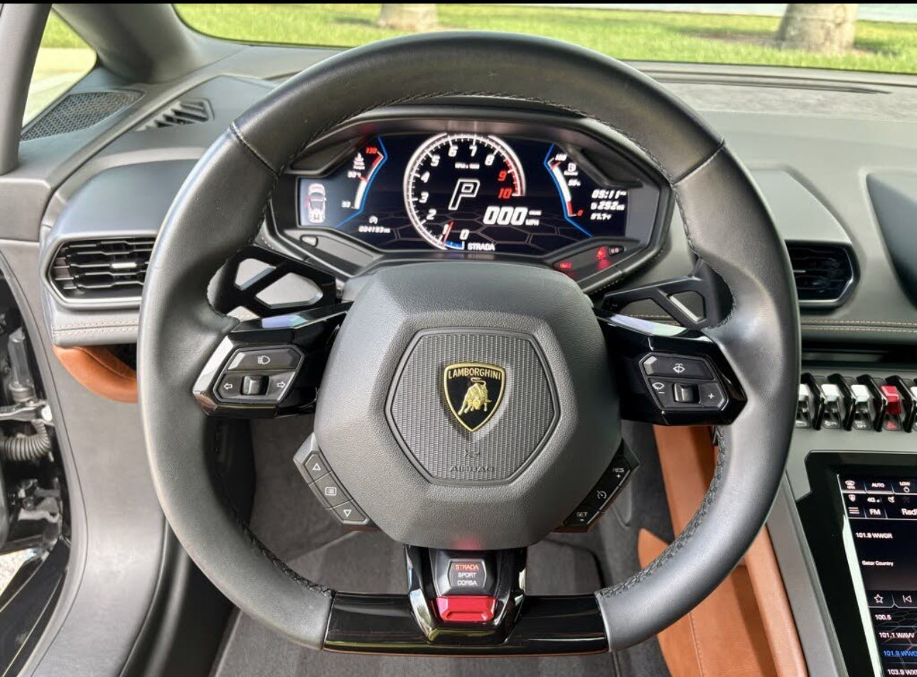 Leather-wrapped Lamborghini steering wheel with multifunction controls and digital dashboard display in luxury sports car interior.