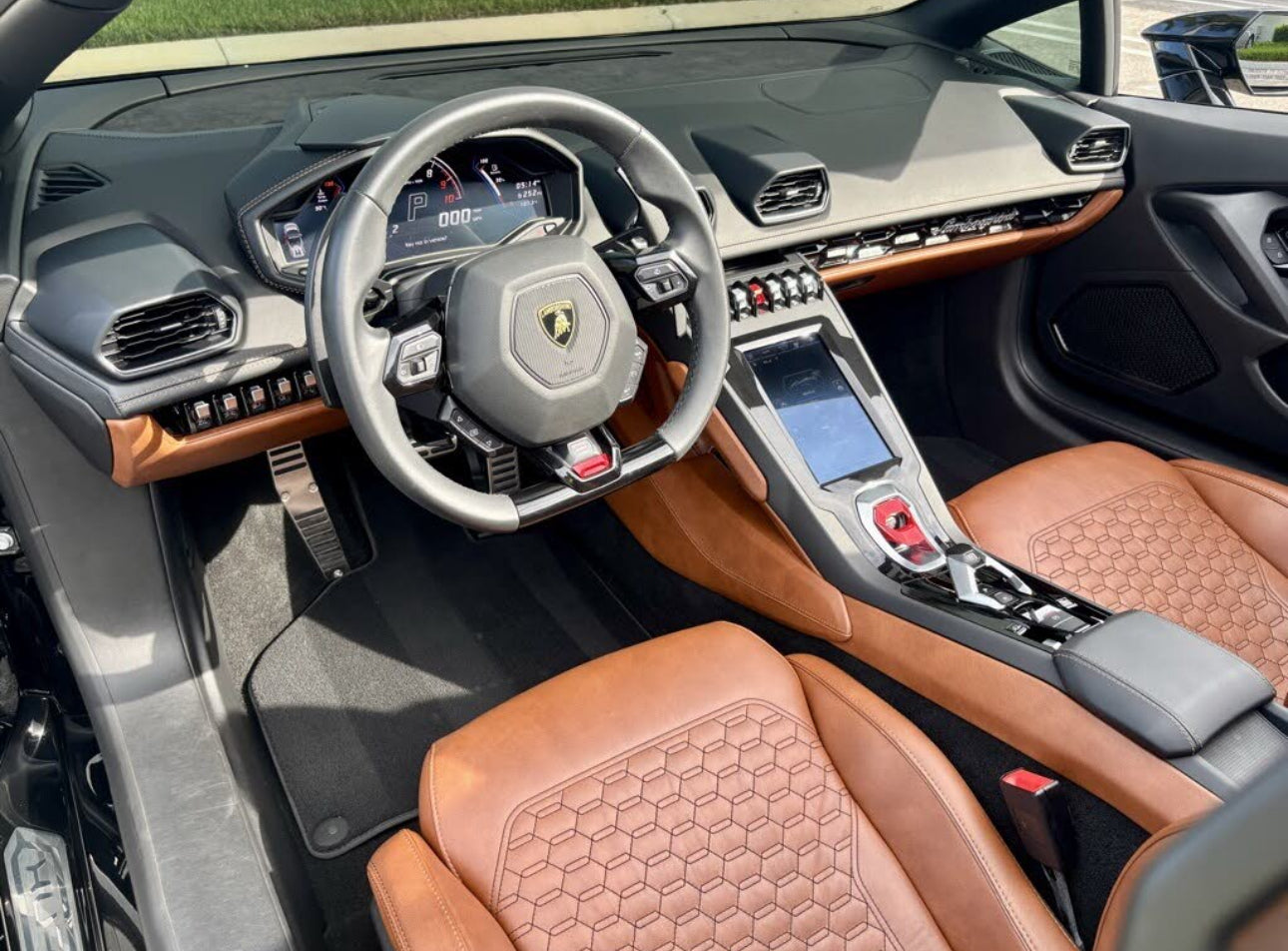 Interior view of luxury Lamborghini sports car featuring premium brown leather seats, black leather-trimmed steering wheel with Lamborghini emblem, digital dashboard, and advanced touchscreen center console.