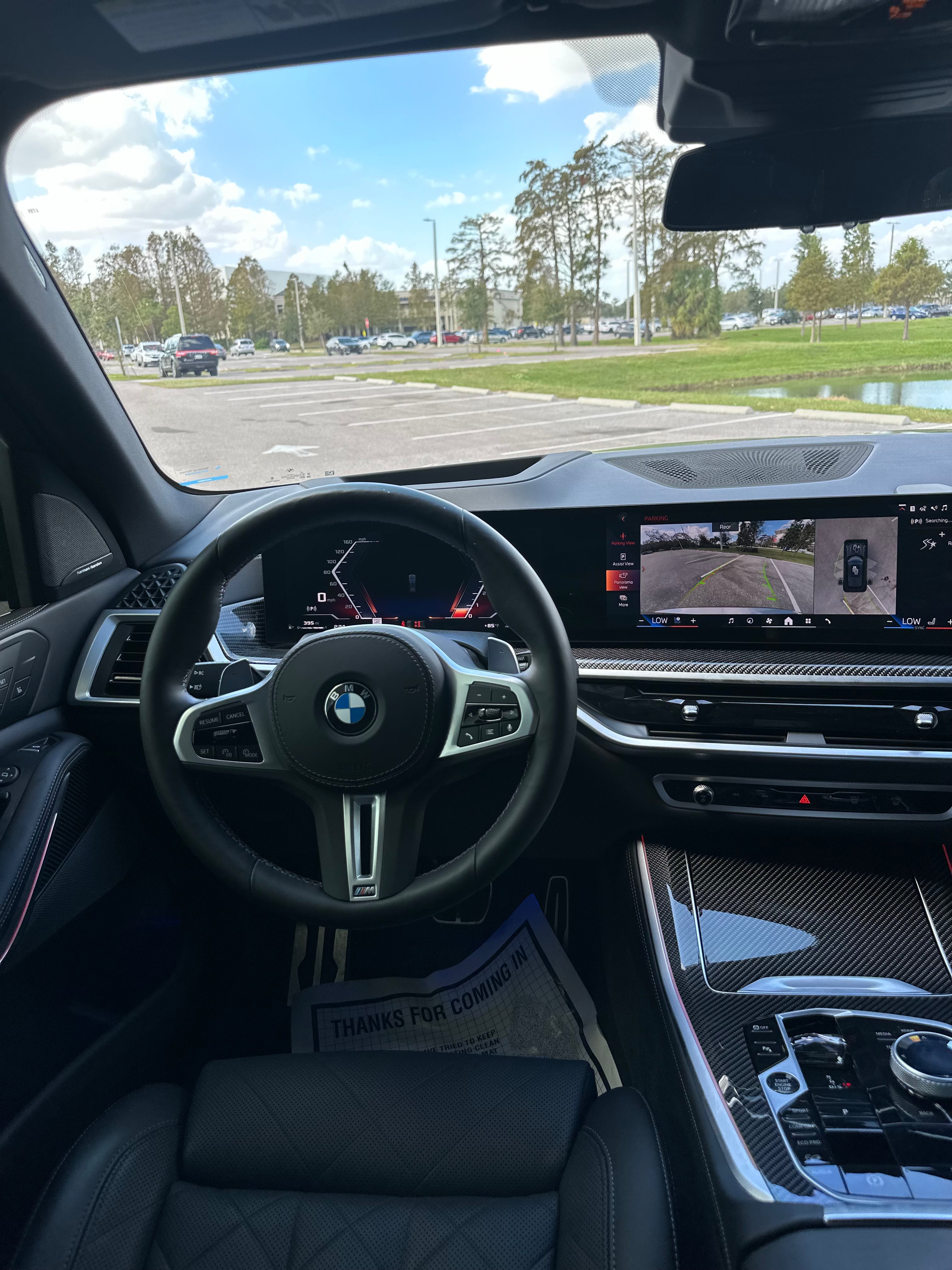 Interior view of BMW M model luxury car featuring leather steering wheel, digital dashboard, advanced navigation screen with parking assist, and carbon fiber center console.