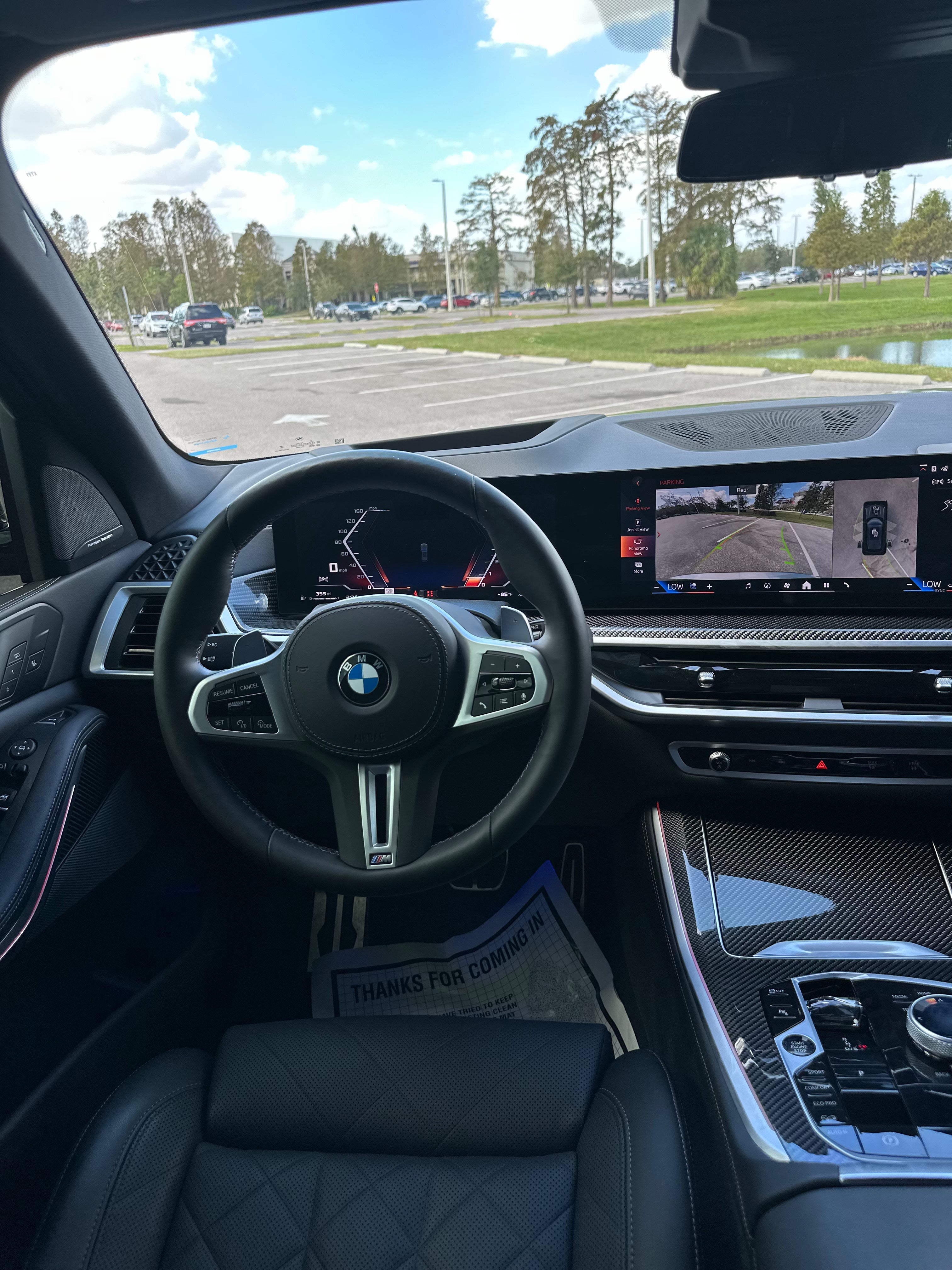 Interior view of BMW M Series luxury car showcasing black leather steering wheel, advanced digital dashboard, and carbon fiber center console with high-tech infotainment and parking assist system.