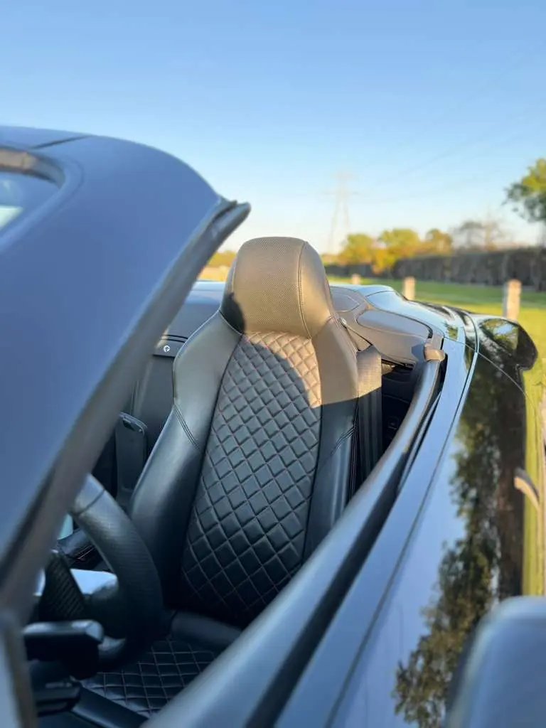 Black quilted leather car seat interior in a luxury convertible sports car with detailed stitching and ergonomic design.