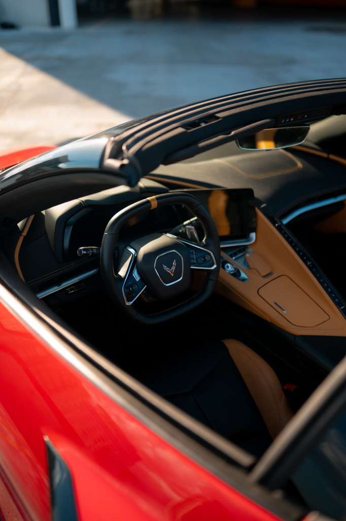 Red convertible sports car interior with black and brown leather seats, modern steering wheel, and touchscreen dashboard display.