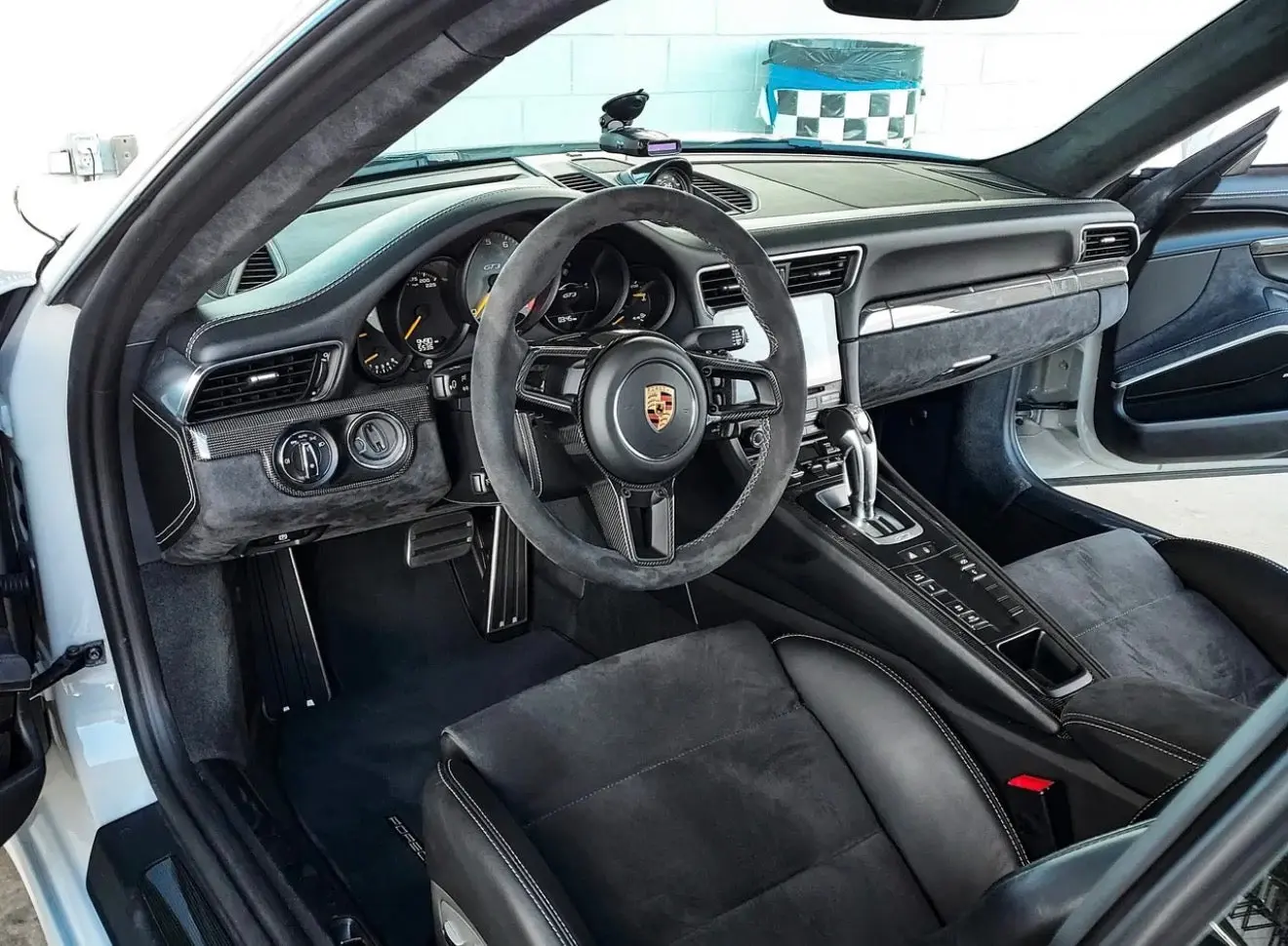 Interior view of a luxury Porsche GT3 sports car featuring black leather and Alcantara seats, sporty steering wheel, and modern dashboard with digital display and carbon fiber accents.