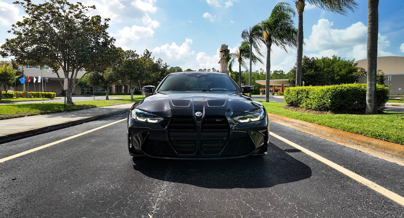 Front view of sleek black BMW M4 parked on asphalt road, showcasing aggressive grille and LED headlights, luxury sports car for sale.