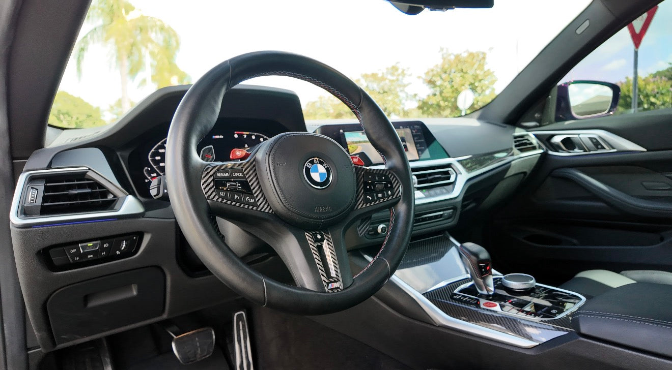 Interior view of a luxury BMW car featuring a black leather steering wheel with carbon fiber accents, digital dashboard, and advanced multimedia control system.