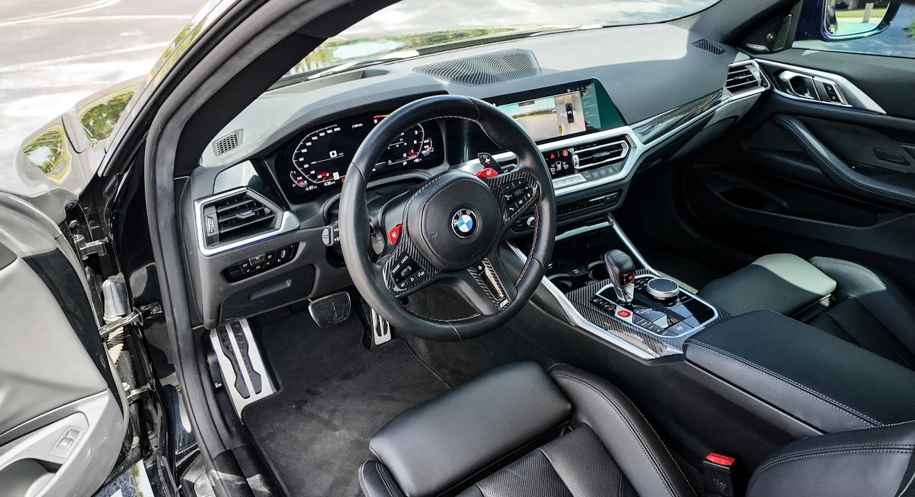 BMW M Series luxury car interior with leather steering wheel, digital dashboard, and carbon fiber trim.