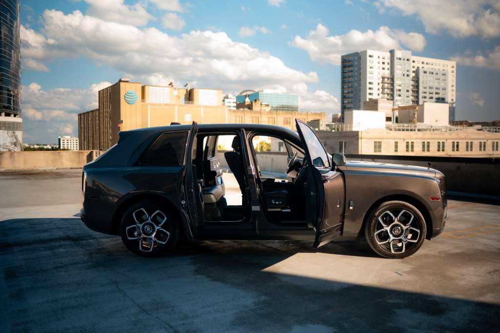 Luxury Rolls-Royce Cullinan SUV in sleek black with open doors, parked on rooftop with city skyline background, premium luxury car for sale.
