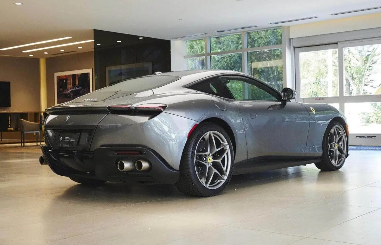 Sleek gray Ferrari Roma luxury sports car rear side view in modern showroom with alloy wheels and dual exhaust.