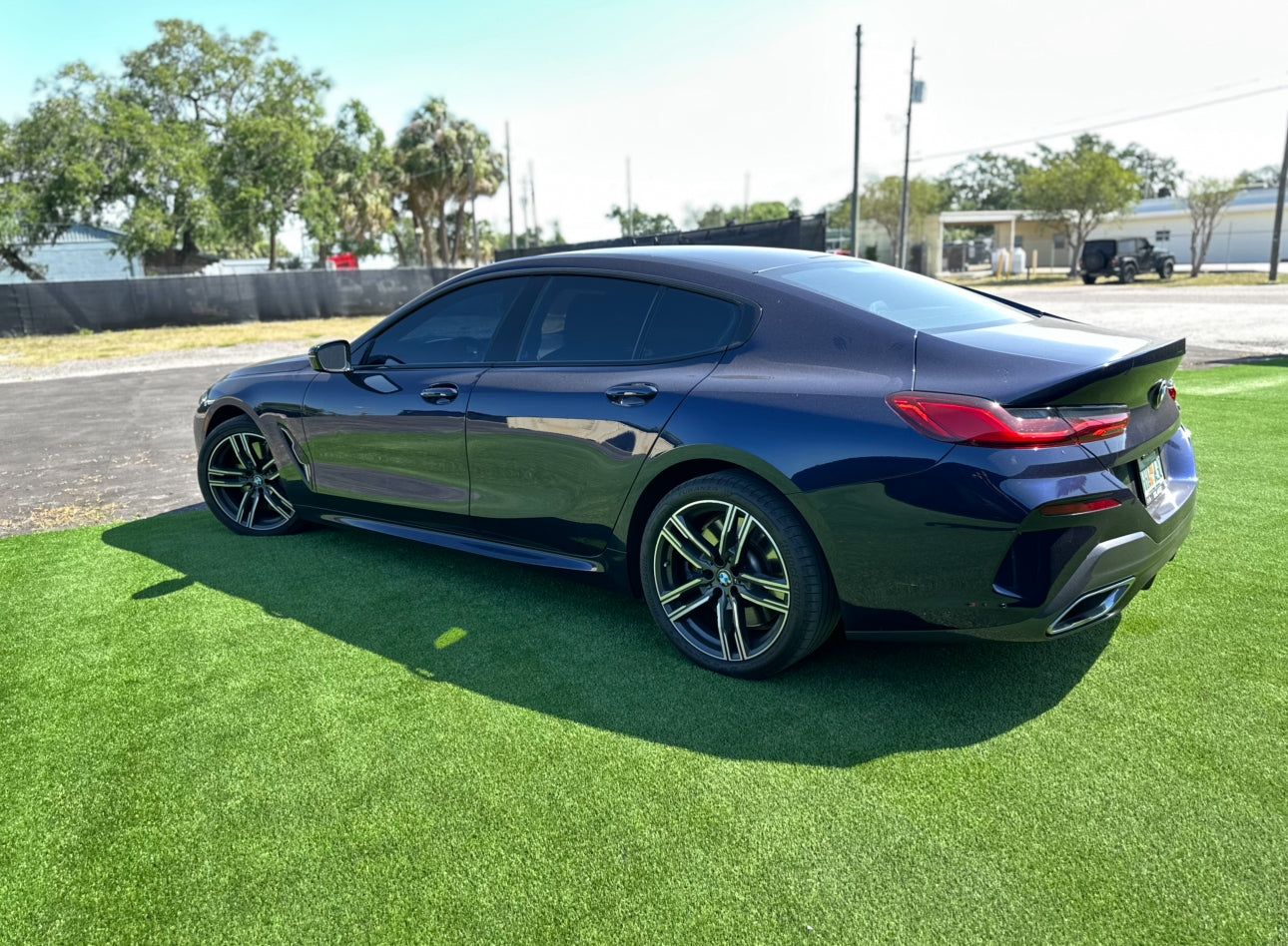 Glossy black BMW 8 Series Gran Coupe luxury sports car with tinted windows and alloy wheels parked on green grass.