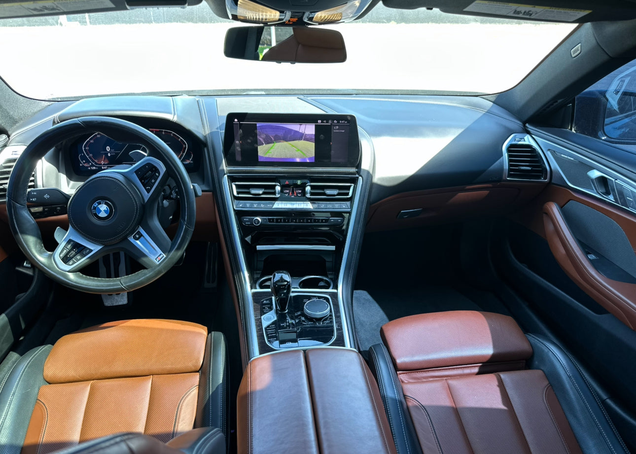 Interior view of luxury BMW car featuring brown leather seats, modern dashboard with digital display, and advanced infotainment system.