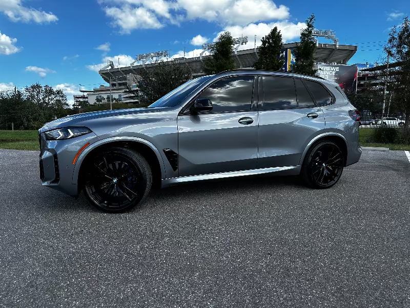 2023 BMW X7 luxury SUV in metallic gray with black alloy wheels parked outdoors under blue sky, premium midsize SUV with sleek design.