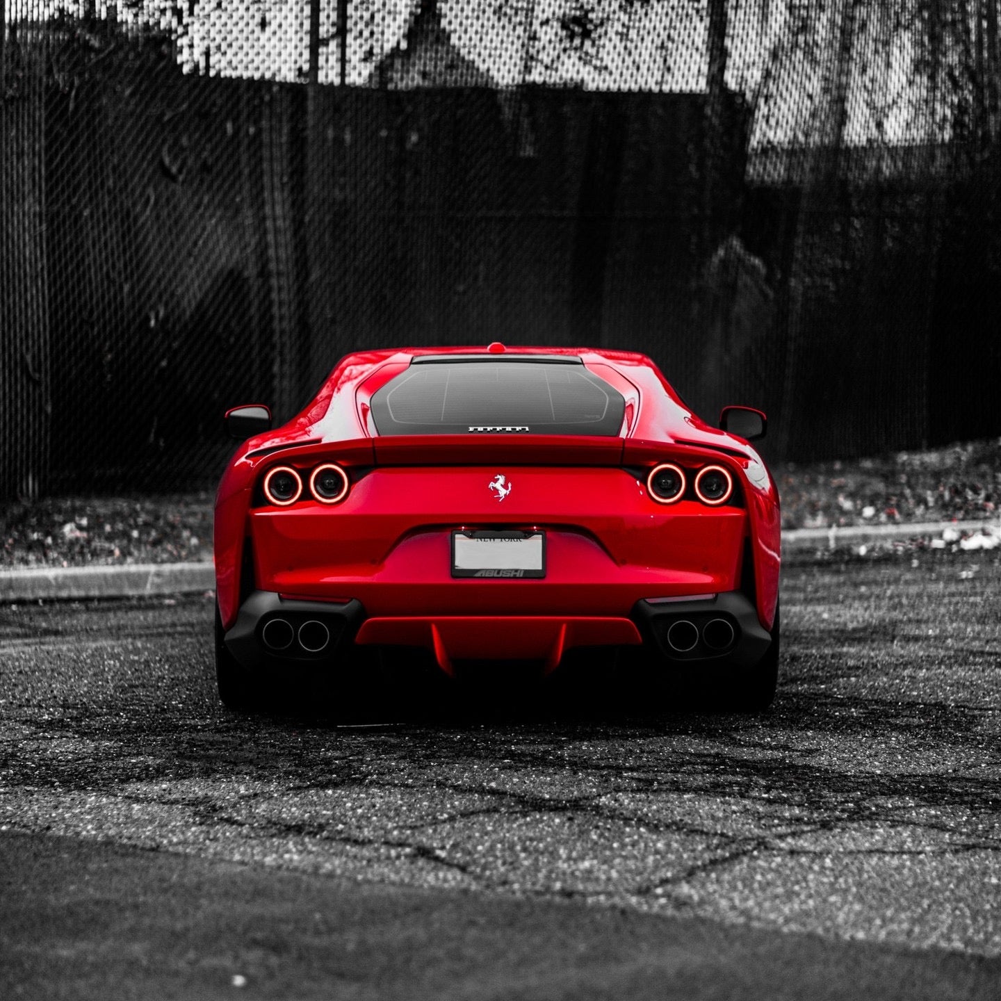 Rear view of a red Ferrari sports car with quad exhaust pipes, sleek aerodynamic design, and distinctive circular taillights on an asphalt road.