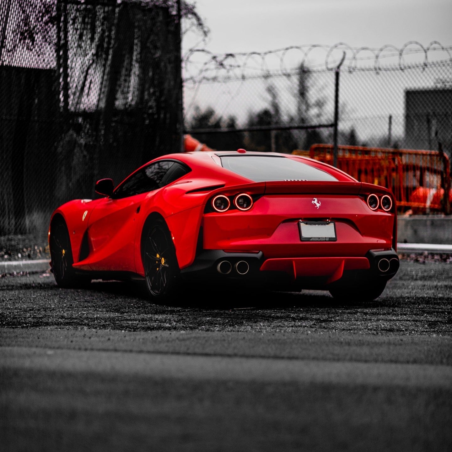 Red luxury Ferrari sports car rear view, high-performance exotic supercar with sleek design and black alloy wheels, parked on asphalt street.