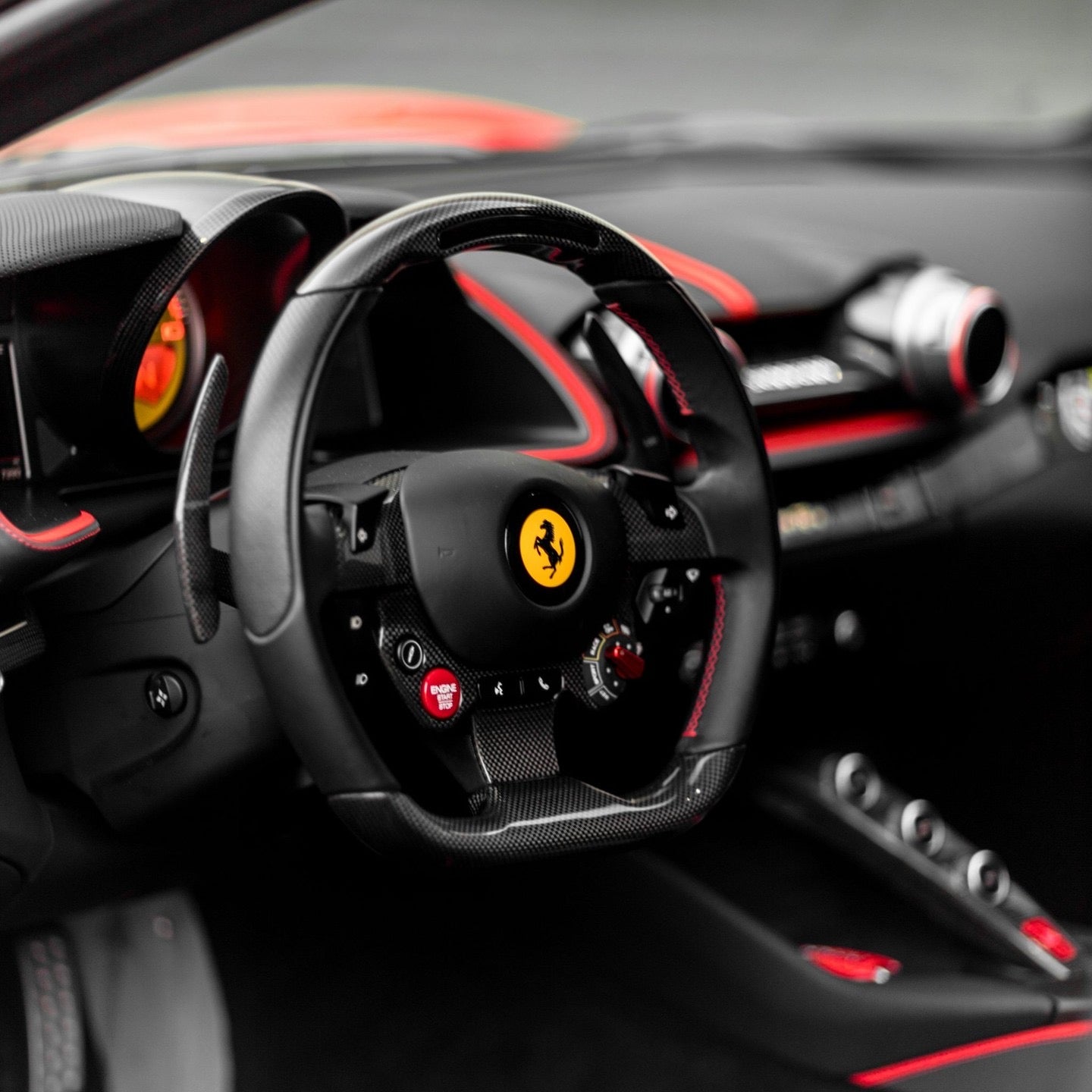 Luxury Ferrari sports car interior with carbon fiber steering wheel, red stitching, and advanced dashboard controls.