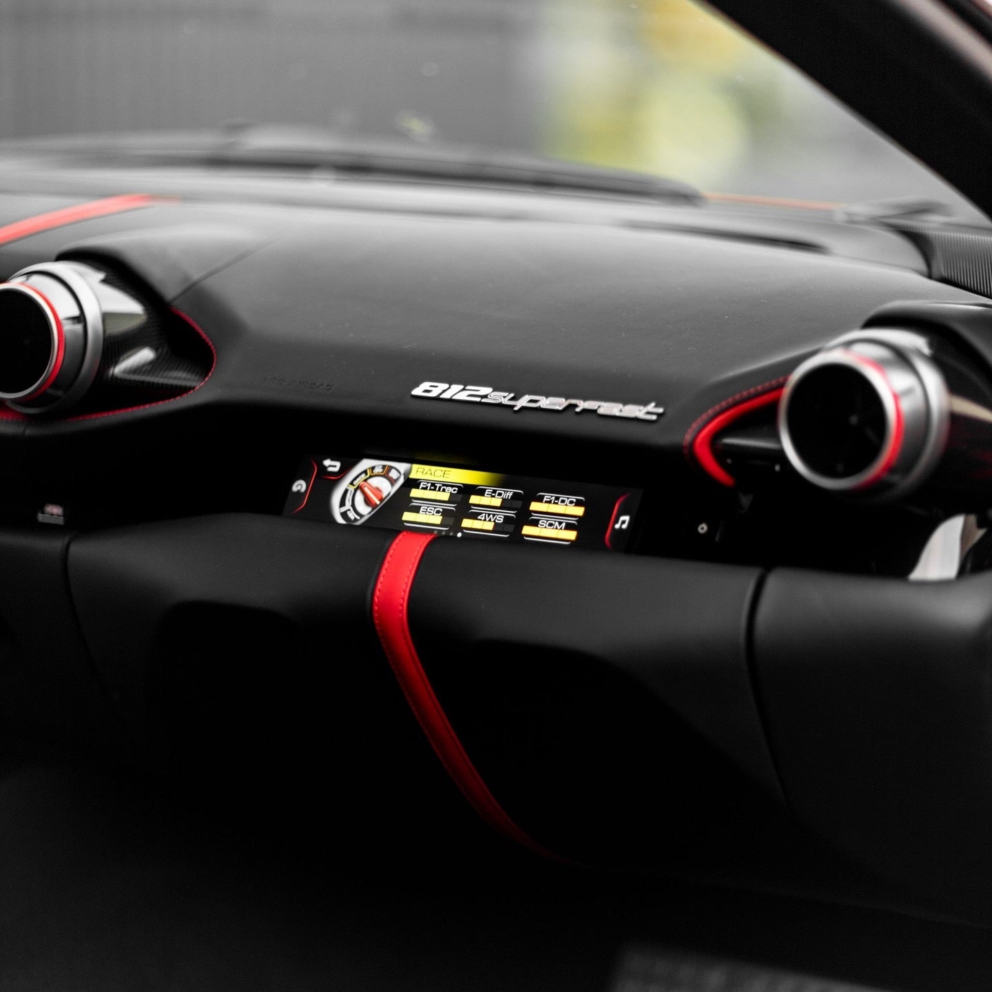 Close-up of Ferrari 812 Superfast dashboard with digital performance controls, black interior, and red leather accents.