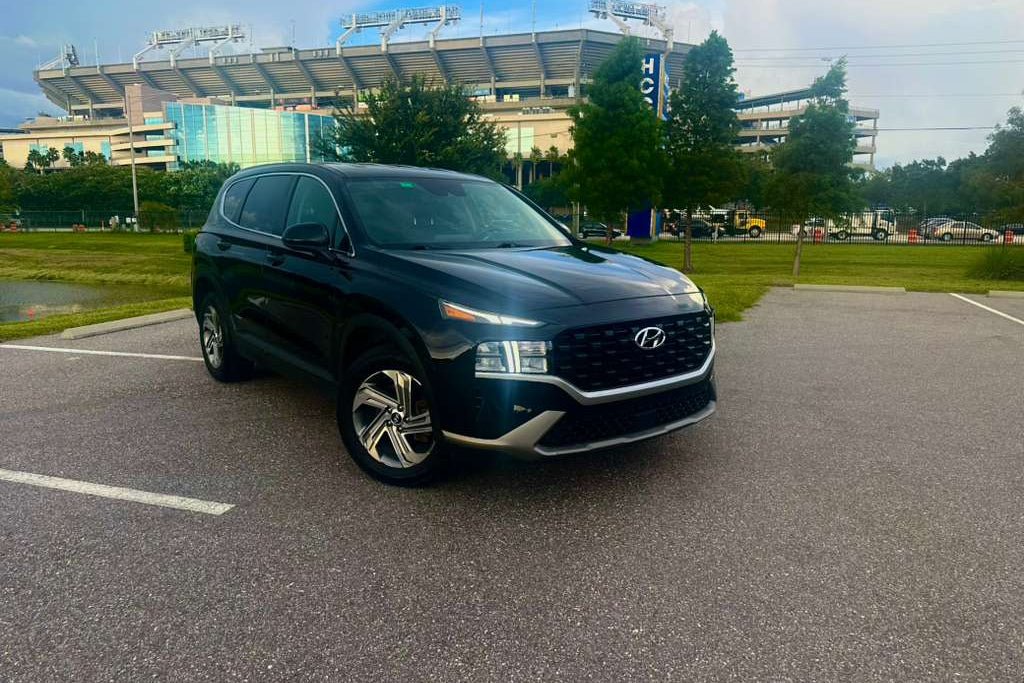 Black 2023 Hyundai Santa Fe SUV parked in an outdoor parking lot, featuring modern LED headlights and alloy wheels, ideal for family and city driving.