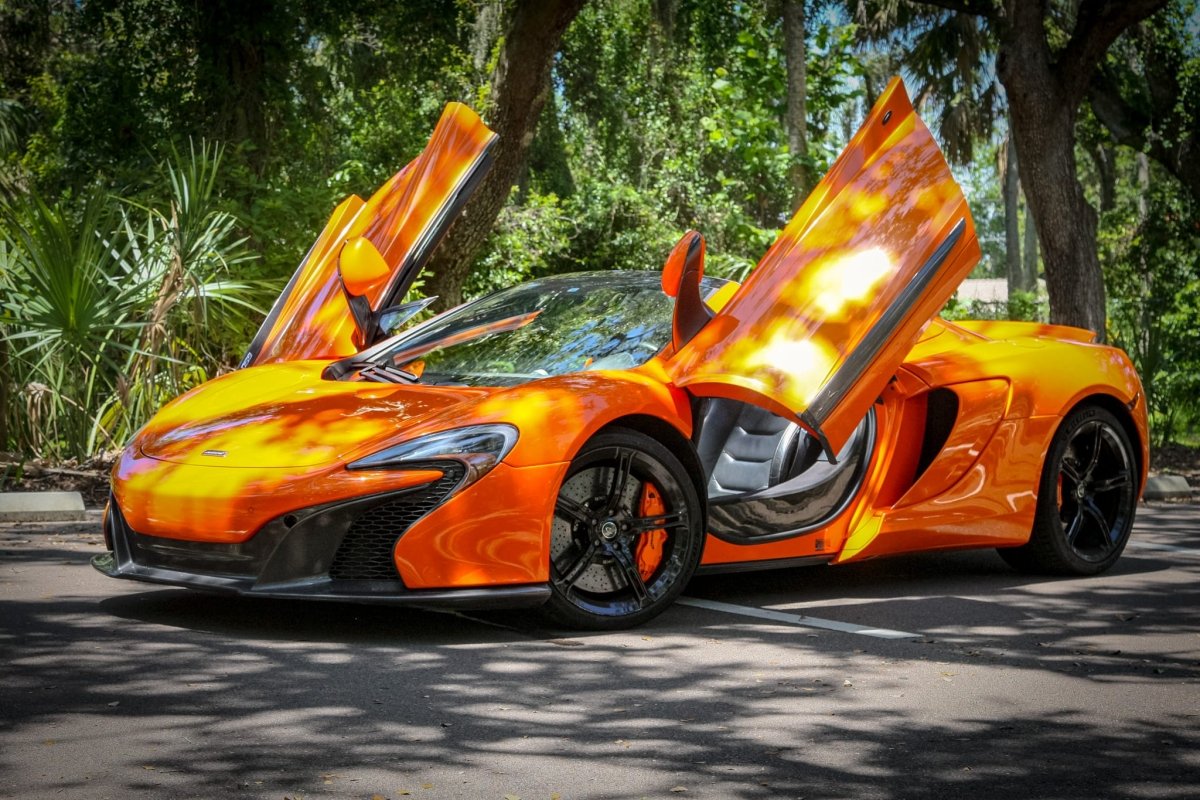 Orange McLaren sports car with butterfly doors open, black alloy wheels, and sleek aerodynamic design parked outdoors, luxury supercar for sale.