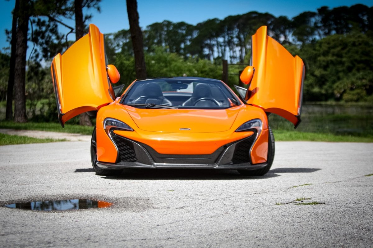 Front view of bright orange luxury sports car with butterfly doors open, showcasing sleek aerodynamic design and black interior, ideal for high-performance driving.