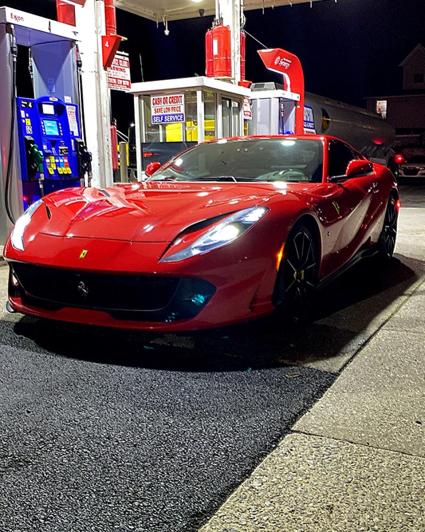 Red luxury Ferrari sports car parked at gas station at night, high-performance exotic vehicle with sleek design and LED headlights.